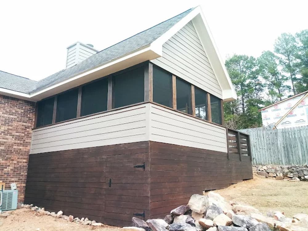 Screened-in porch addition with wooden siding and stone landscaping in a residential setting.